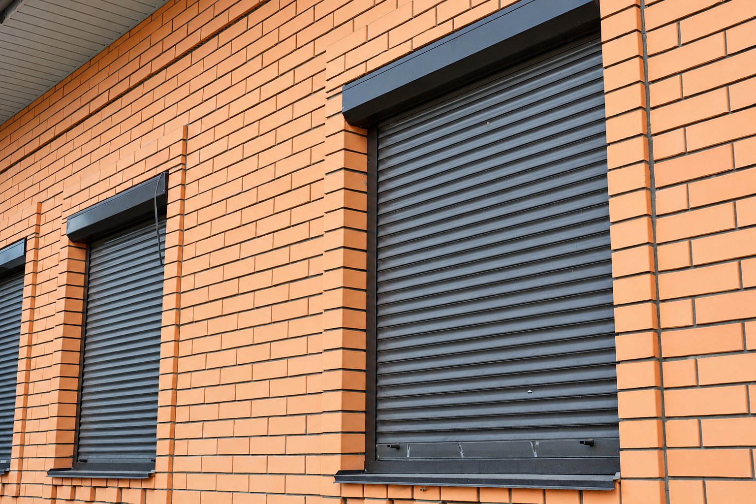 Façade de maison en briques orange équipée de fenêtres avec volets roulants bruns fermés.